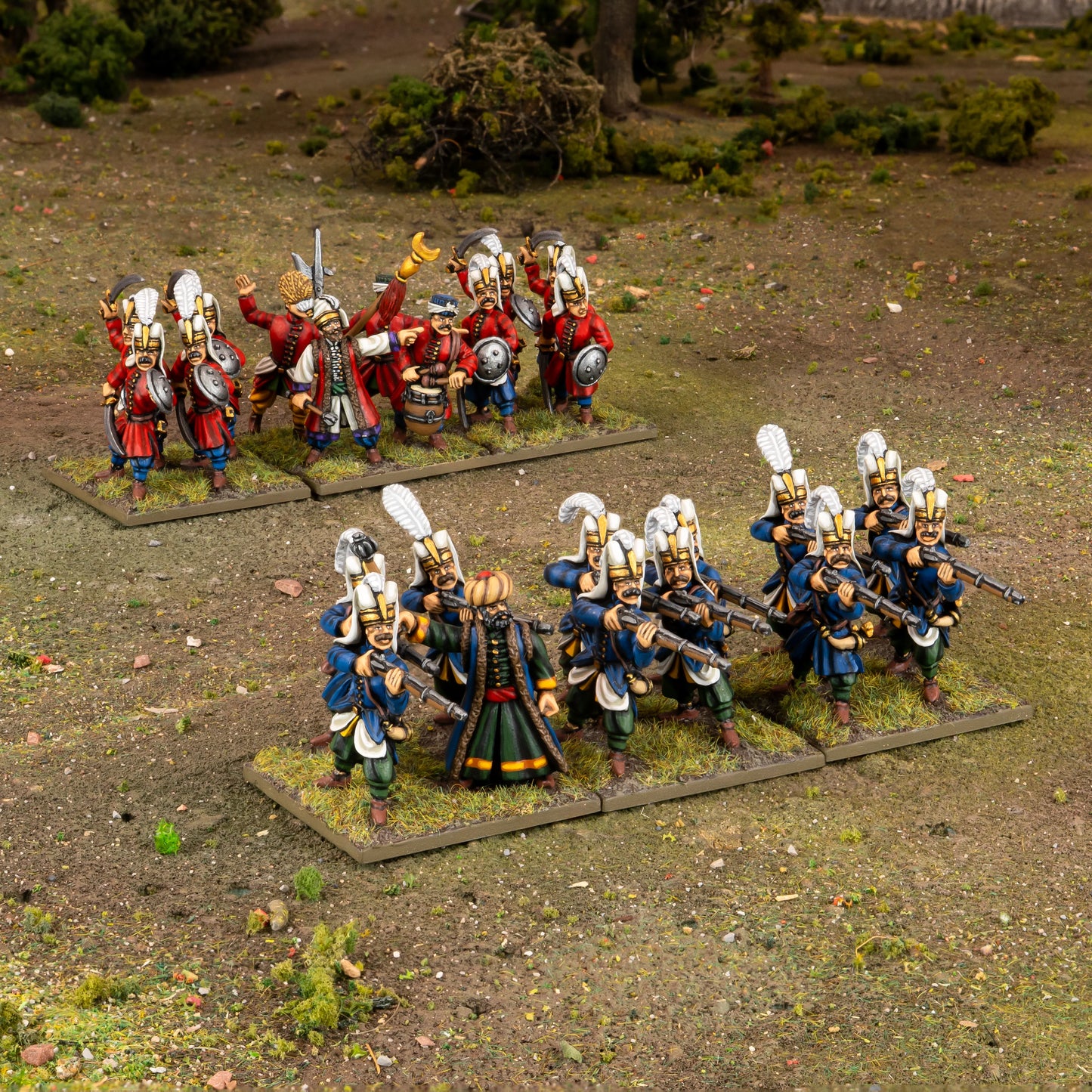 Warlord Games Ottoman Janissaries Regiment – diorama na stole: podstawka szermierzy w czerwonych mundurach i podstawka strzelców w niebieskich mundurach na trawiastym terenie 28mm Pike & Shotte