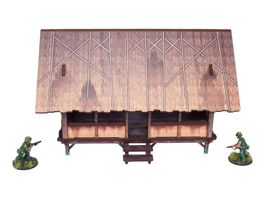 WW2 Pacific Kitchen (1) PREPAINTED – zmontowana kuchnia dżunglowa na palach, widok z przodu: otwarty budynek z dachem ze strzechy w rombowy wzór i bambusowymi ścianami, dwie figurki żołnierzy 28mm Bolt Action, białe tło