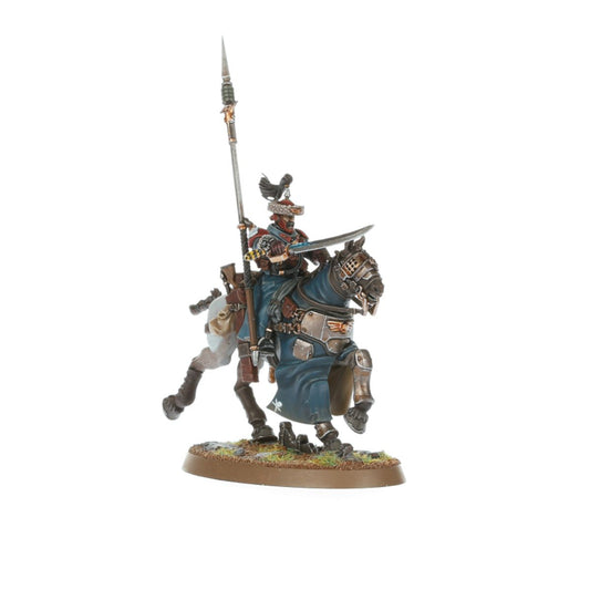Attilan Rough Rider Sergeant - widok z lewej niebieski płaszcz z białym symbolem czaszki szaro-brązowa zbroja hunting lance z srebrnym ostrzem pionowo szabla z szerokim srebrnym ostrzem srebrny hełm z czarnym pióropuszem i czerwoną opaską czarny koń z szarą zbroją i niebieskim czaprakiem Astra Militarum Warhammer 40000