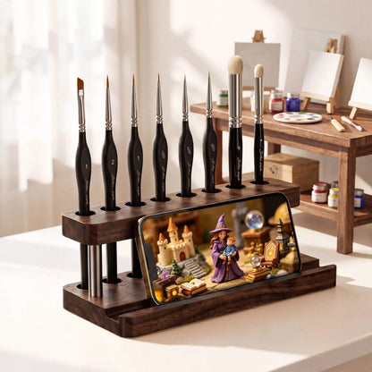 2-in-1 Paint Brush Holder & Phone Stand Golden Maple – lifestyle: drewniany organizer z ciemnego drewna orzechowego z 7 pędzlami Golden Maple (rozmiary 1, 2, 1, 3/0, 3/0, liner, 5) ustawionymi pionowo w otworach górnej belki; w rowku podstawy smartfon wyświetlający scenę fantasy z czarodziejką i zamkiem; w tle miniaturowe biurko malarskie z paletą i farbami
