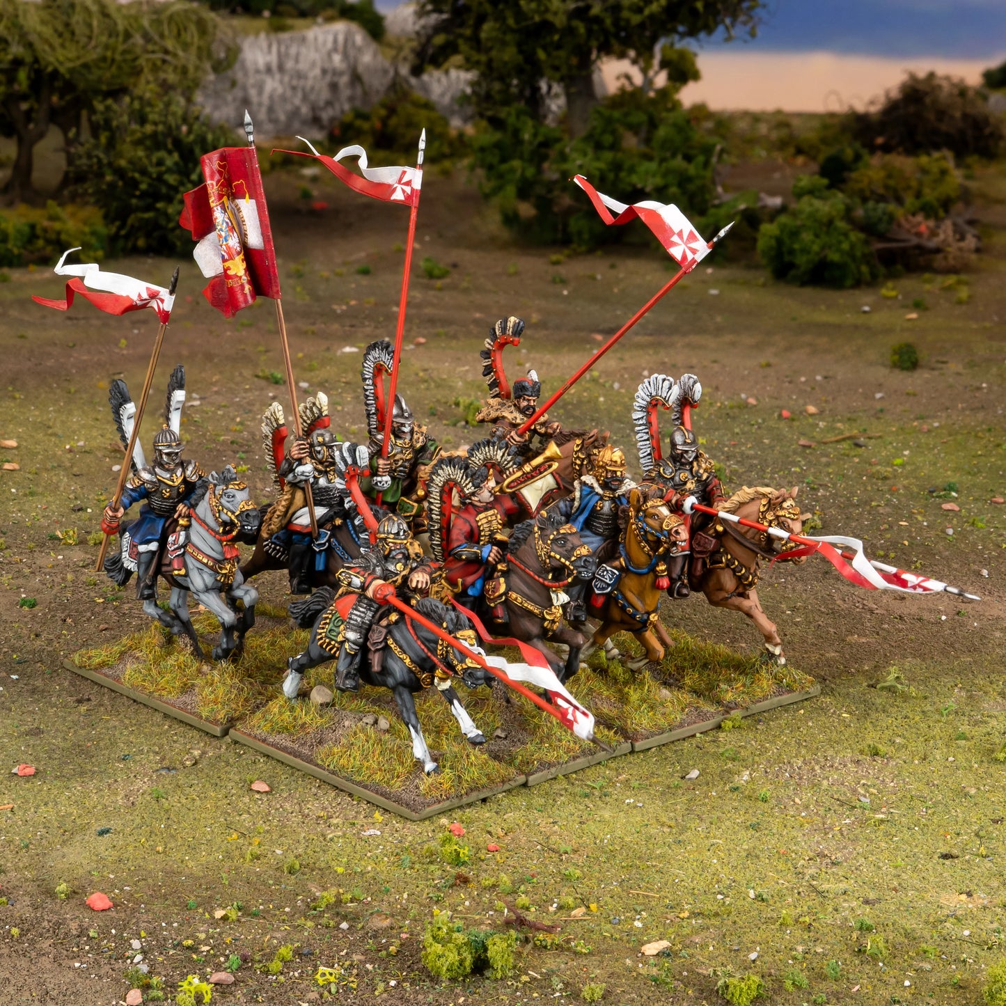 Warlord Games Polish Winged Hussars Regiment – diorama na terenie: 8 Husarzy Skrzydlatych w szarży na trawiastym polu z drzewami i skałami w tle 28mm Pike & Shotte