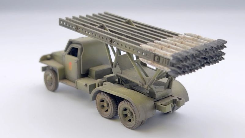 Rubicon Models 280036 BM-13N Katiusza – zmontowany i pomalowany model plastikowy 1/56 28mm widok z boku-tyłu: Studebaker US6 6x6 w oliwkowej zieleni z czerwoną gwiazdą na drzwiach, wyrzutnia rakiet M-13 uniesiona pod kątem z rakietami na szynach, koła terenowe 6x6, białe tło, Bolt Action