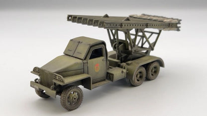 Rubicon Models 280036 BM-13N Katiusza – zmontowany i pomalowany model plastikowy 1/56 28mm widok z boku-przodu: Studebaker US6 6x6 w oliwkowej zieleni z czerwoną gwiazdą na drzwiach, wyrzutnia rakiet M-13 uniesiona pod kątem, szyny startowe z rakietami, koła terenowe 6x6, białe tło, Bolt Action