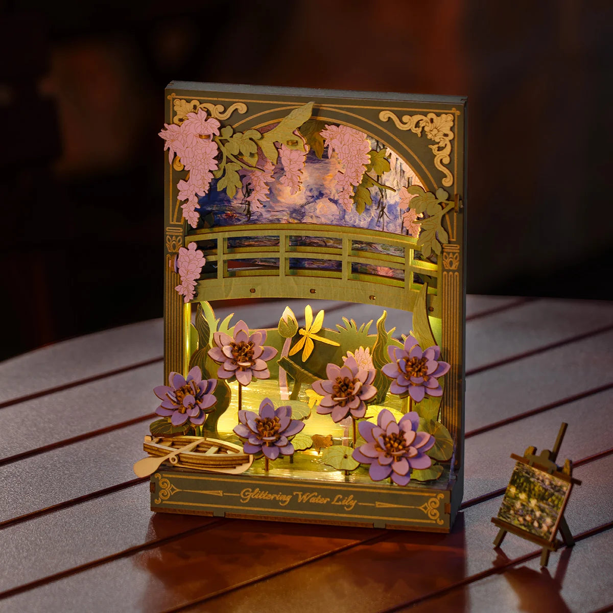 Lilie Wodne Glittering Water Lily Rowood TH001 – gotowy model z włączonym LED na drewnianym stole, ciepłe złote światło oświetla lilie i staw