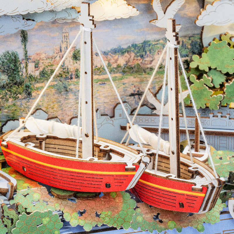 Czerwone Łodzie Red Boats Rolife TH004 – ręka pisząca pocztówkę obok gotowego obrazu 3D na drewnianym biurku z liśćmi