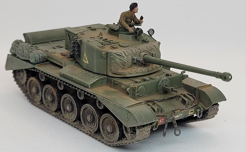 Rubicon Models 280094 A34 Comet – zmontowany i pomalowany model plastikowy 1/56 28mm: brytyjski czołg szybki Comet w oliwkowej zieleni z żółtym trójkątem i numerem 52 na wieży, armata 77mm HV, figurka dowódcy w otworze wieży, gąsienice stalowe, wyposażenie na kadłubie, widok z boku-przodu, białe tło, Bolt Action