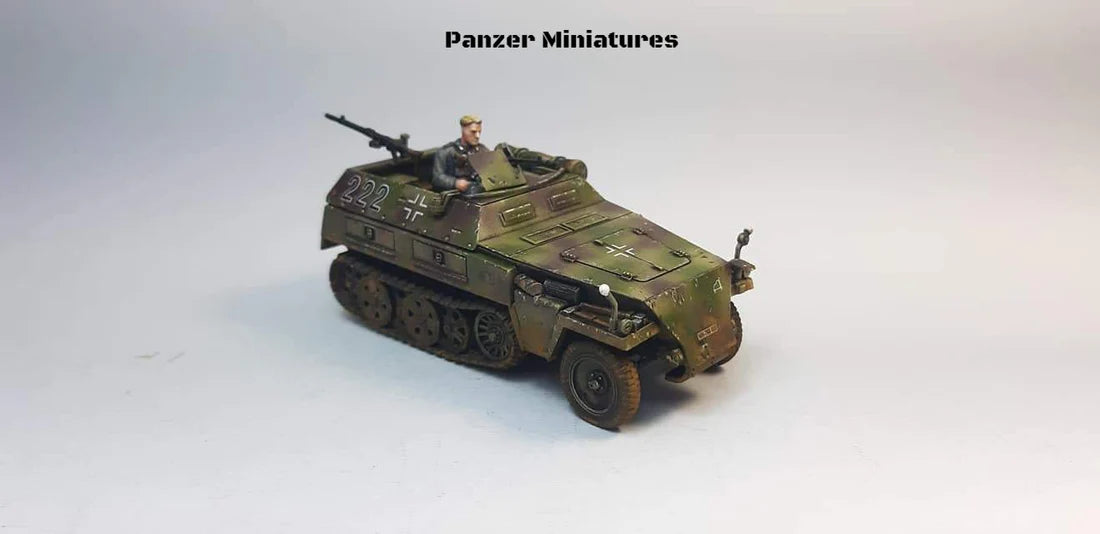 Rubicon Models 280038 SdKfz 250/1 Neu – zmontowany i pomalowany model plastikowy 1/56 28mm widok z boku-przodu: transporter opancerzony w trójkolorowym kamuflażu (oliwkowy, brązowy, piaskowy) z numerem 222 i krzyżem żelaznym na kadłubie, figurka strzelca przy MG 34, gąsienice stalowe, koła przednie, białe tło, Bolt Action