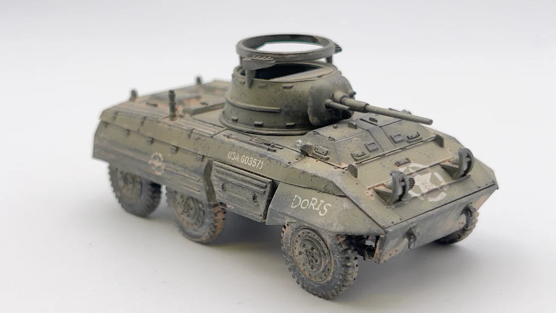 Rubicon Models 280028 M8 Greyhound – zmontowany i pomalowany model plastikowy 1/56 28mm widok z tyłu-boku: amerykański samochód pancerny w pustynnym kamuflażu piaskowym z białą gwiazdą i numerem USA 3018913 na kadłubie, armata 37mm M6 w wieży, pierŜień MG, koła terenowe 6x6, białe tło, Bolt Action