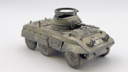 Rubicon Models 280028 M8 Greyhound – zmontowany i pomalowany model plastikowy 1/56 28mm widok z tyłu-boku: amerykański samochód pancerny w pustynnym kamuflażu piaskowym z białą gwiazdą i numerem USA 3018913 na kadłubie, armata 37mm M6 w wieży, pierŜień MG, koła terenowe 6x6, białe tło, Bolt Action
