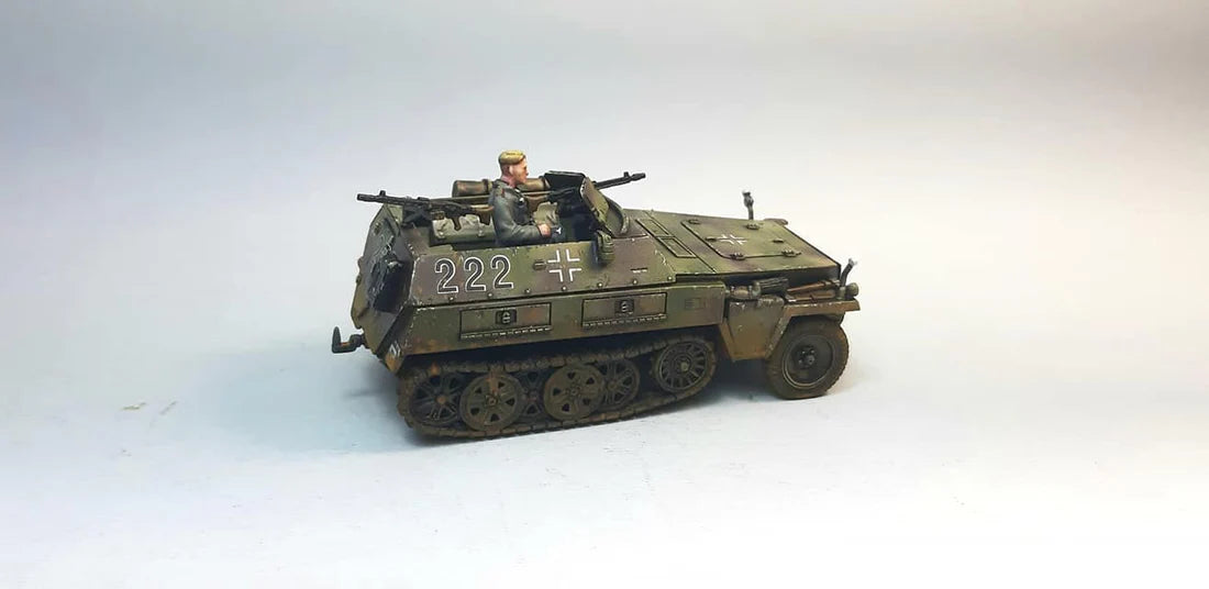 Rubicon Models 280038 SdKfz 250/1 Neu – zmontowany i pomalowany model plastikowy 1/56 28mm widok z tyłu-boku: transporter opancerzony w trójkolorowym kamuflażu (oliwkowy, brązowy, piaskowy) z numerem 222 i krzyżem żelaznym na kadłubie, figurka strzelca przy MG 34, tylne drzwi, gąsienice stalowe, białe tło, Bolt Action