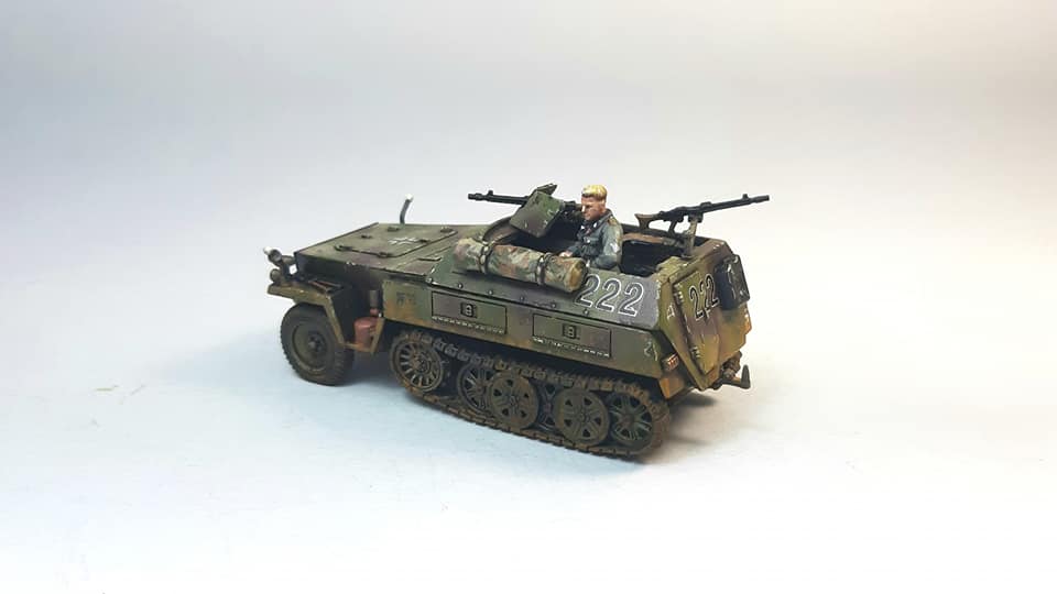 Rubicon Models 280038 SdKfz 250/1 Neu – zmontowany i pomalowany model plastikowy 1/56 28mm widok z boku-przodu: transporter opancerzony w oliwkowym kamuflażu z numerem 222 i krzyżem żelaznym na kadłubie, figurka strzelca przy MG 34 i MG 34 z tyłu, gąsienice stalowe, koła przednie, białe tło, Bolt Action