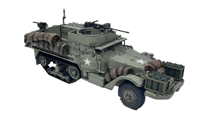 Rubicon Models 280027 M3 / M3A1 Half-Track – zmontowany i pomalowany model plastikowy 1/56 28mm widok z boku-przodu: amerykański transporter półgąsienicowy M3A1 w pustynnym kamuflażu piaskowym z białą gwiazdą i numerem USA 4015042 na masce, karabin maszynowy M2HB na pierścieniu, tylne stojaki bagażowe otwarte, gąsienice stalowe, koła przednie, białe tło, Bolt Action