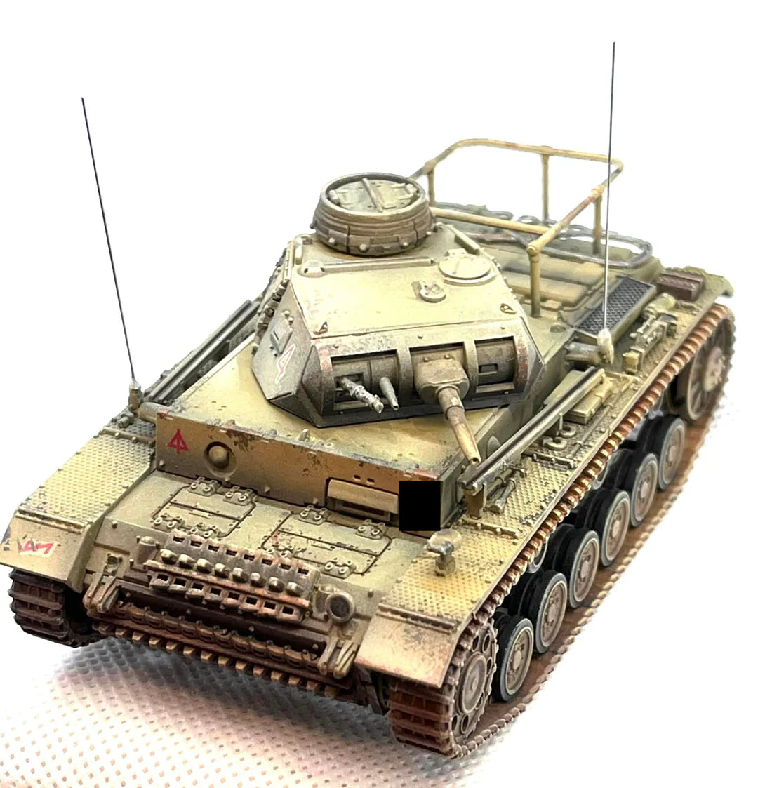 Rubicon Models 280091 Panzer III Ausf. E/F/G – zmontowany i pomalowany model plastikowy 1/56 28mm widok z góry-przodu: PzKpfw III Ausf G w pustynnym kamuflażu piaskowym z czerwonym trójkątem na kadłubie, armata 37mm KwK 35/36, dwa karabiny maszynowe MG 34 w wieży, właz dowódcy otwarty, anteny radiowe, gąsienice stalowe, białe tło, Bolt Action