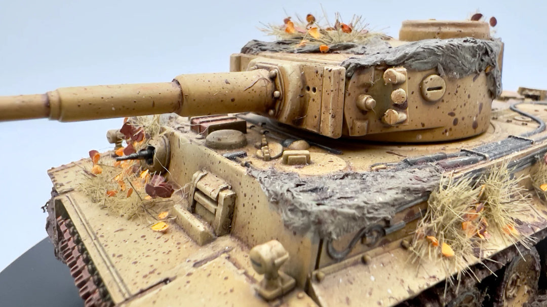 Rubicon Models 280016 Tygrys I Ausf. E – zmontowany i pomalowany model plastikowy 1/56 28mm widok z góry-przodu: czołg ciężki Tygrys I w pustynnym kamuflażu piaskowym z efektem weatheringu (błoto, rdza, pył), armata KwK 36 L/56 kal. 88mm, wieża z włazem, gąsienice stalowe, suche trawy i liście na modelu, białe tło, Bolt Action