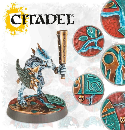 Citadel Shattered Dominion podstawki - jaszczuroludzki wojownik z maczugą na ozdobnej podstawce 32mm z czerwono-turkusowym wzorem ruin i złotymi detalami, obok 4 przykładowe podstawki z motywem Shattered Dominion - Warhammer Age of Sigmar