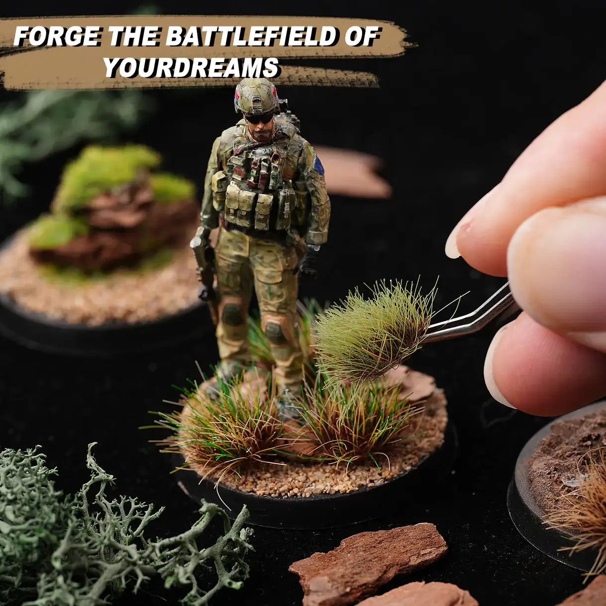 Battlefield Basing Set Golden Maple – zbliżenie na dłoń umieszczającą pęsetą kępę trawy Swamp Tufts na podstawce figurki żołnierza nowoczesnego; wokół materiały do baz: mech Shrubbery, kamienie korowe, kępy trawy; napis "Forge the Battlefield of Your Dreams"
