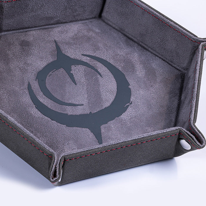 Malediction Premium Dice Tray – zbliżenie na szare logo Malediction wytłoczone na ciemnoszarej zamszowej powierzchni tacy z czerwonymi szwami na białym tle