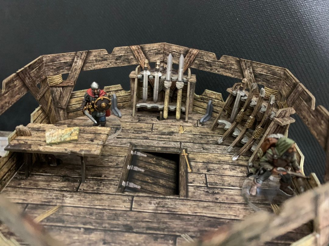 Watchtower BSTFWE008 28-35mm Battle Systems - wnętrze górnego piętra stojaki na broń miecze figurki walczące widok z góry ciemne tło
