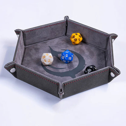 Malediction Premium Dice Tray – sześciokątna taca na kości rozłożona z 4 kośćmi D20 (żółta, niebieska, biała, czarna) na szarej powierzchni z logo Malediction na jasnym tle