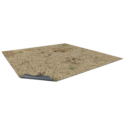 Mata do gry bitewnej Desert Wasteland 60x60 cm (2'x2') – widok z perspektywy: kwadratowa mata z nadrukiem spieczonej, spękanej pustynnej ziemi w odcieniach piaskowych i brązowych z nielicznymi kępami suchej trawy i śladami po pociskach, zagięty róg ukazuje szary spodni materiał antypoślizgowy, białe tło, Bolt Action, Warhammer 40000