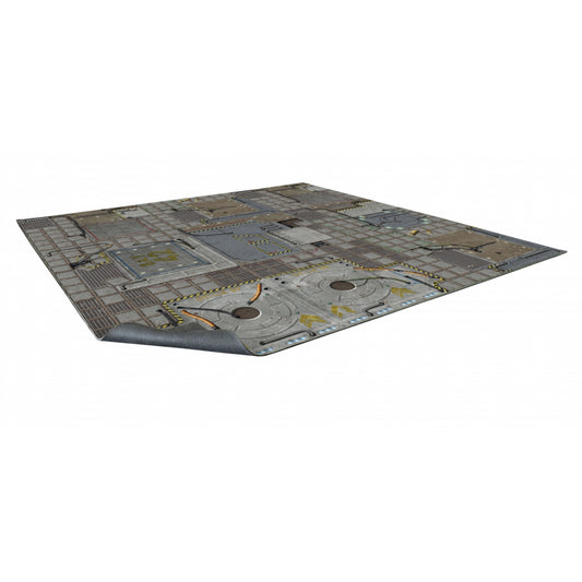 Mata do gry bitewnej Frontier Sci-Fi 60x60 cm (2'x2') – widok z perspektywy: kwadratowa mata z nadrukiem futurystycznej platformy kosmicznej w odcieniach szarych i stalowych z żółto-czarnymi pasami ostrzeżenia, okrągłymi włazami, kablami, panelami technologicznymi i kratownicami, zagięty róg ukazuje szary spodni materiał antypoślizgowy, białe tło, Warhammer 40000, Kill Team, Core Space