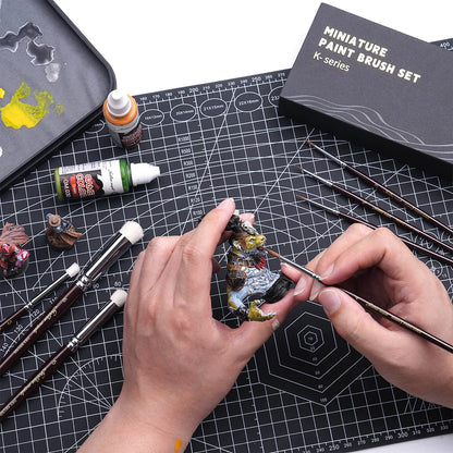 Malowanie figurki smoka pędzlem detalizującym Golden Maple K-Series – pędzle i pudełko K-Series na czarnej macie do cięcia, farby Game Color obok
