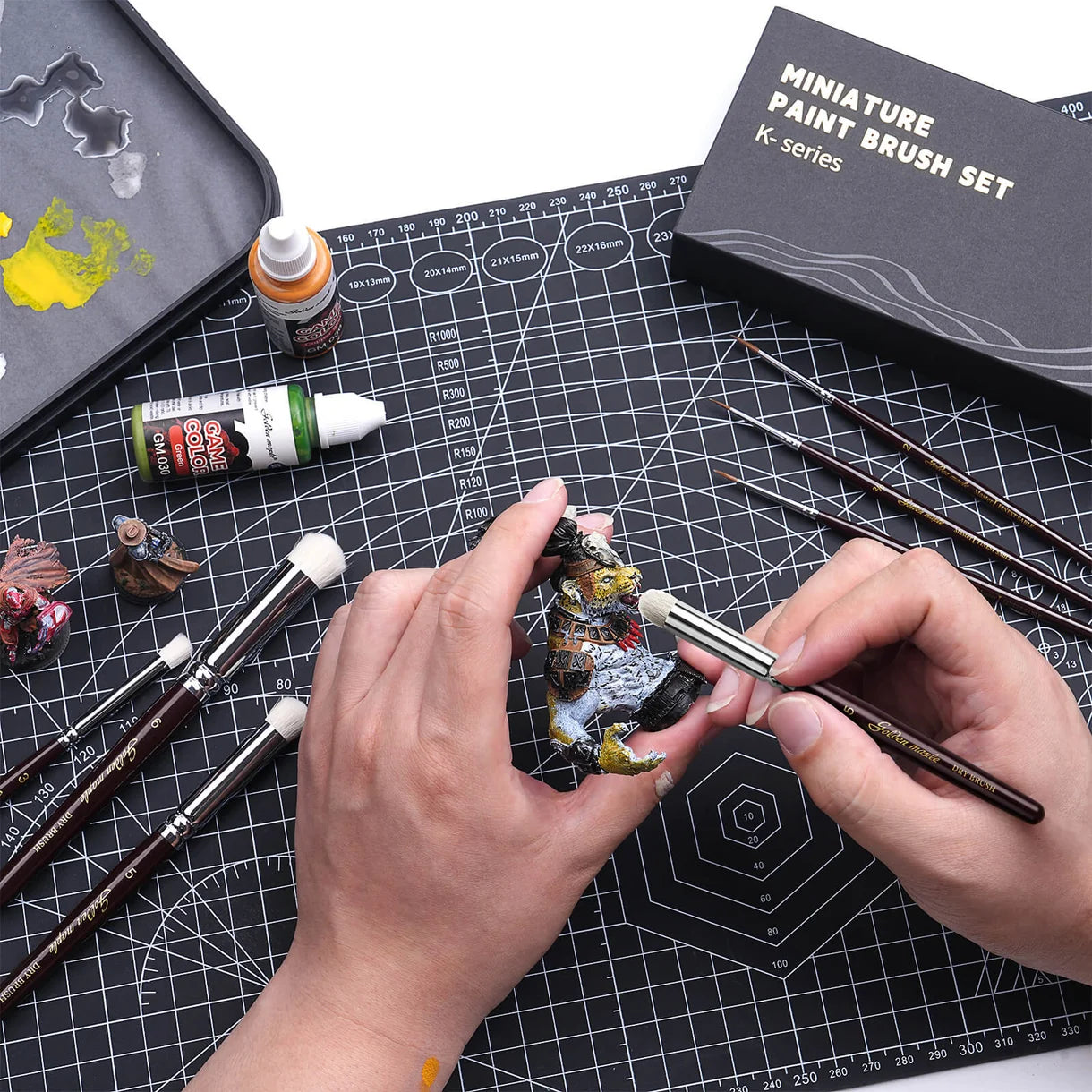 Dry brushing figurki smoka pędzlem Golden Maple Dry Brush – pędzle K-Series i pudełko Miniature Paint Brush Set na czarnej macie
