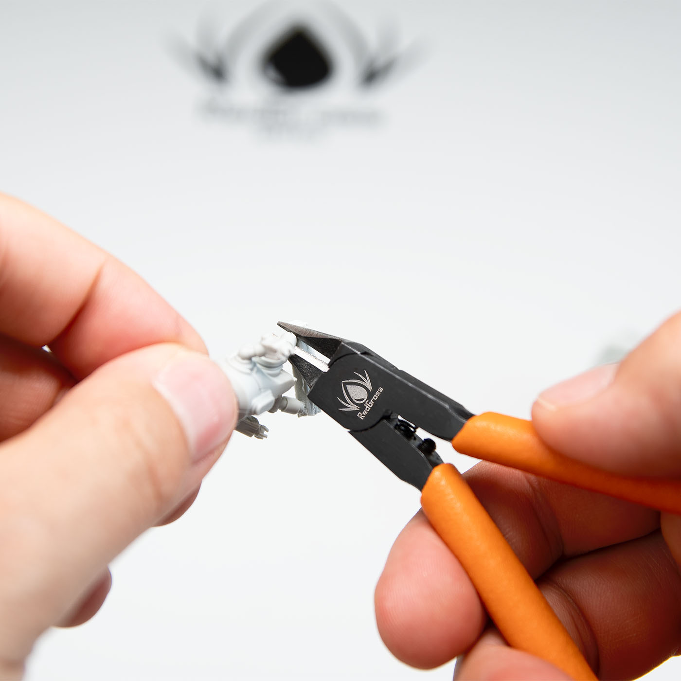 Redgrass Sprue Cutters – zbliżenie na cięcie figurki z wypraski obiema rękami, logo Redgrass w tle
