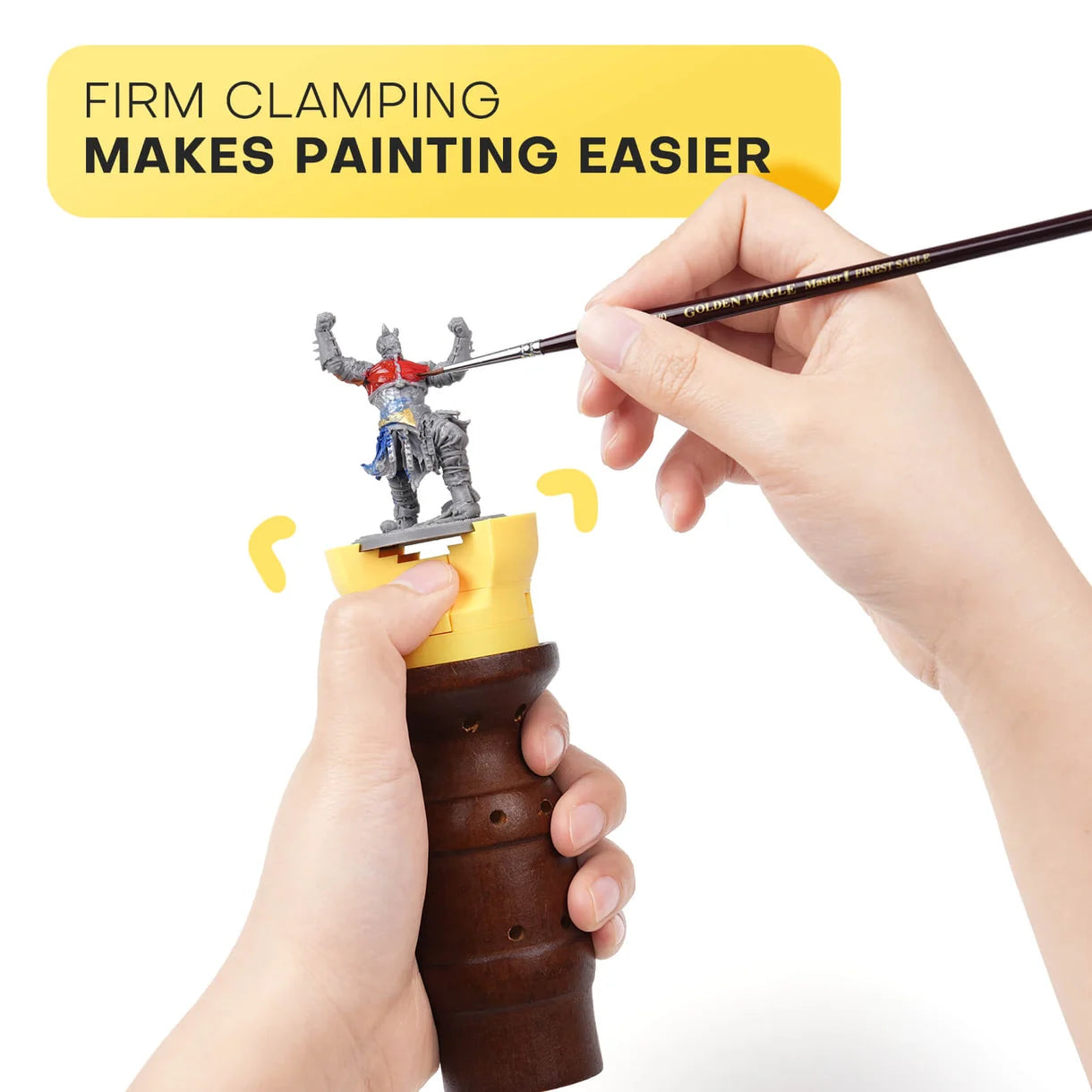 Głowica zaciskowa Golden Maple trzymana w dłoniach podczas malowania figurki Warhammer pędzlem Kolinsky – napis "Firm Clamping Makes Painting Easier"
