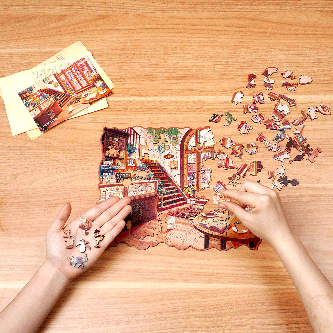 Przytulna Zimowa Kawiarnia Rowood TA006 Cozy Winter Café – ręce układające puzzle na drewnianym stole z rozrzuconymi elementami o unikalnych kształtach i naklejką referencyjną