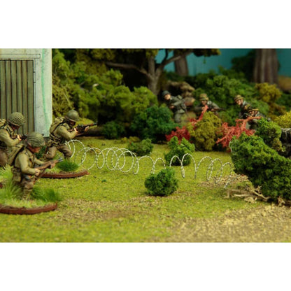 Warlord Games Barbed Wire WG-TER-47 – drut kolczasty użyty jako przeszkoda terenowa na stole do gry: spirale drutu kolczastego na zielonej macie z figurkami piechoty brytyjskiej i niemieckiej w tle, skala 28mm Bolt Action