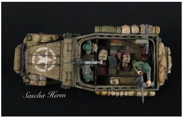 Rubicon Models 280083 M3A1 Scout Car – model 1/56 28mm widok z tyłu-góry: pustynny kamuflaż piaskowy z białą gwiazdą na tylnej płycie, 3 figurki załogi, strzelec przy M2 HMG, łańcuch holowniczy, wyposażenie na burtach, czarne tło, Bolt Action