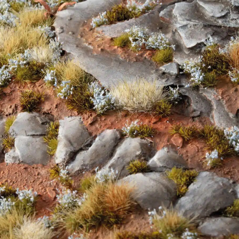 Forget-Me-Not Tiny Flowers 4mm Gamers Grass - diorama skalna z czerwoną ziemią i kamieniami pokryta drobnymi niebieskimi kępkami niezapominajek wśród traw
