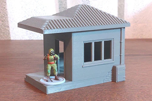 Guard Hut pomalowany – widok z przodu z gankiem i oknem, figurka w środku, teren 28mm Patrick Miniatures
