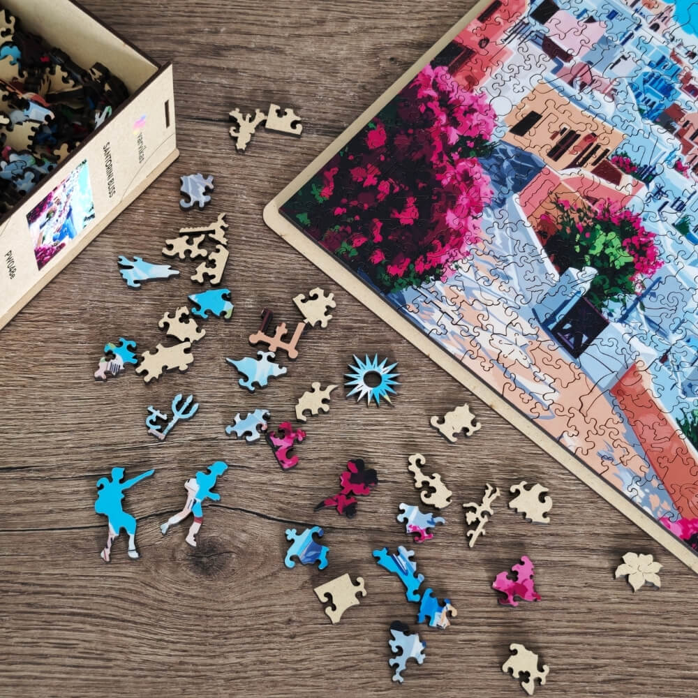 Drewniane puzzle Santorini Bliss Värvikas PW048e – rozsypane figurkowe elementy na drewnianym stole obok częściowo ułożonego obrazu: tancerz, trójząb, słońce, kwiaty i inne kształty
