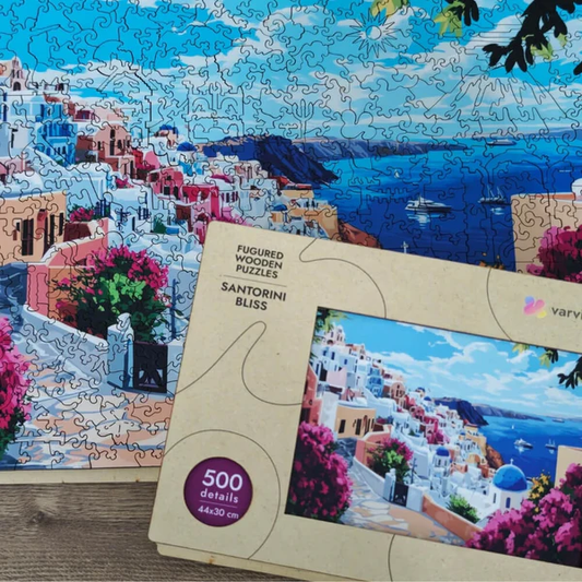 Drewniane puzzle Santorini Bliss Värvikas PW048e – prawie ukończony obraz 44×30 cm z widokiem na Santorini z niebieską kopułą i różową bugenwillą, obok pudełko Varvikas
