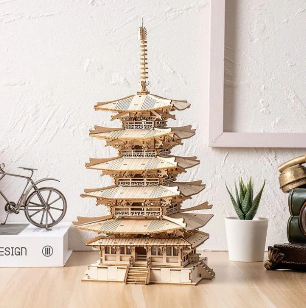 Drewniany puzzle 3D Pięciopiętrowa Pagoda Rolife RK013e – ukończony model na drewnianym biurku obok roweru, sukulenta i książek
