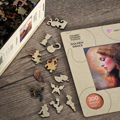 Drewniane puzzle Złota Gracja Värvikas PW051e – pudełko Golden Grace obok rozsypanych figurkowych elementów na drewnianym stole: klepsydra, liść, aniołek, kot i inne kształty
