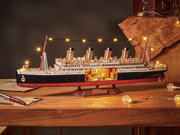 Drewniany puzzle 3D 1912 Eternal Atlantic Voyager Rolife TGL02 – ukończony model na drewnianym stole z podświetlonym wnętrzem i światłami LED na olinowaniu, w tle mapa i szklane kule