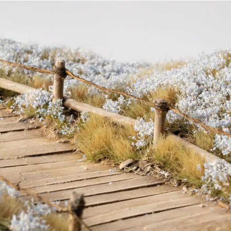 Light Blue Lilac Flowers 6mm Gamers Grass - diorama z drewnianym mostem otoczonym niebiesko-liliowymi kępkami kwiatowymi na łące, zbliżenie na realistyczną teksturę włókien
