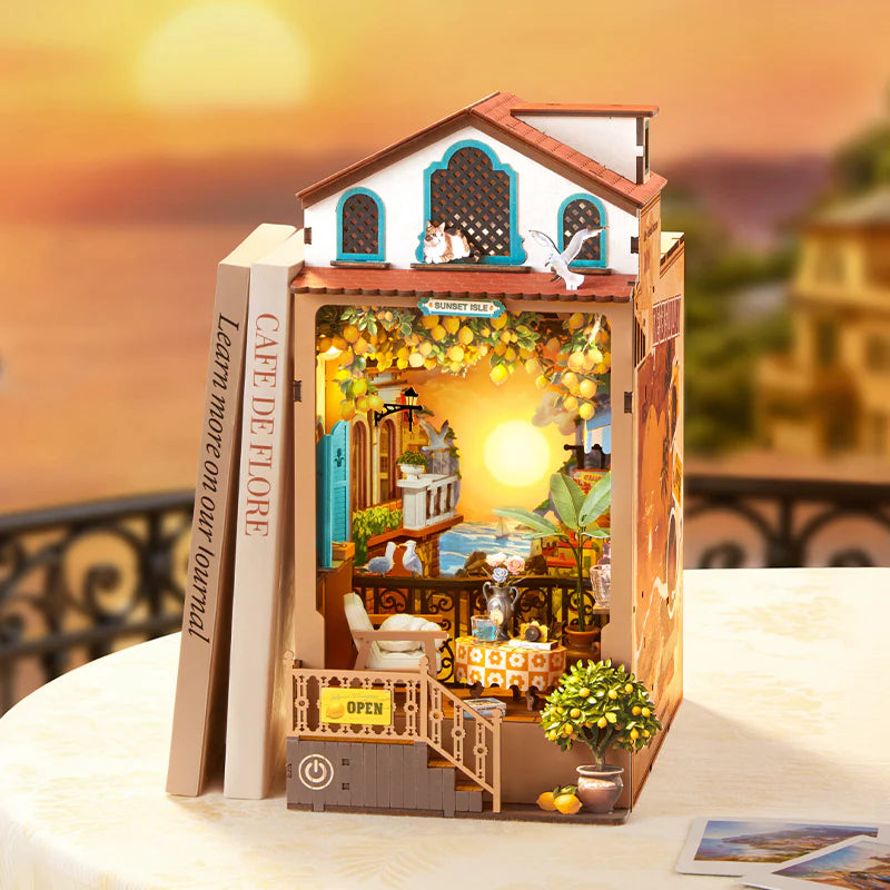Sunset Isle Rolife TGB18 – ilustracja panoramy nadmorskiego miasteczka z latarnią i żółtą żaglówką na tle złotego nieba