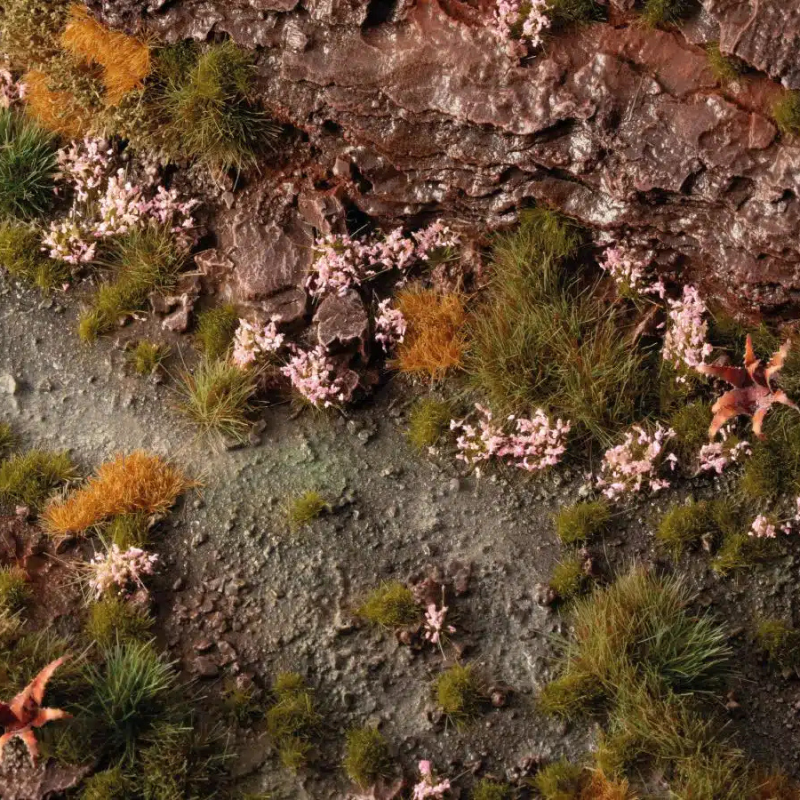 Pink Orchid Tiny Flowers 4mm Gamers Grass - diorama skalna z brunatną ziemią i kamieniami pokryta drobnymi różowymi kępkami storczyka wśród zielonej i rudej trawy
