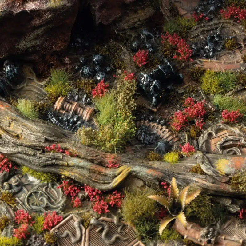 Poppy Tiny Flowers 4mm Gamers Grass - diorama fantasy z korzeniami drzew, czarnymi żywicowymi figurkami i czerwonymi kępkami maku wśród zielonej trawy i szczątków

