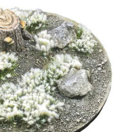 Frosted Snow Tufts 6mm Green Green Stuff World - zbliżenie na okrągłą podstawkę z kępkami zielonej trawy pokrytej szronem, kamieniami i pniakiem
