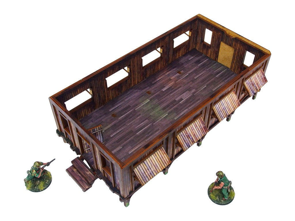 WW2 Pacific Barracks (1) PREPAINTED – koszary dżunglowe ze zdjętym dachem, widok wnętrza z góry pod kątem: UV-drukowana podłoga z desek i bambusowe ściany z otworami okiennymi, dwie figurki żołnierzy 28mm, białe tło
